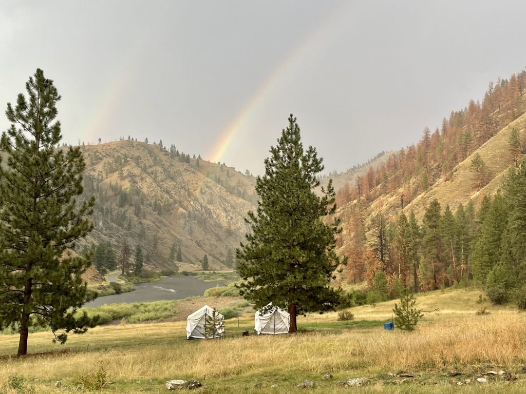 Glamping tents set up in Idaho wilderness with a rainbow overhead