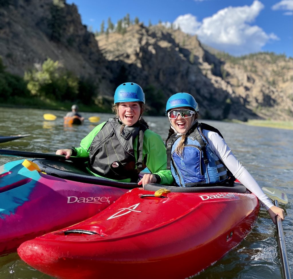 Two girls smiling while sitting in kayaks on the Salmon River in Idaho