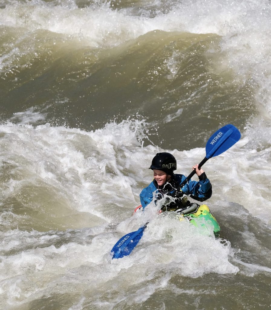 Youth kayaker navigating splashing rapids in Idaho wilderness.