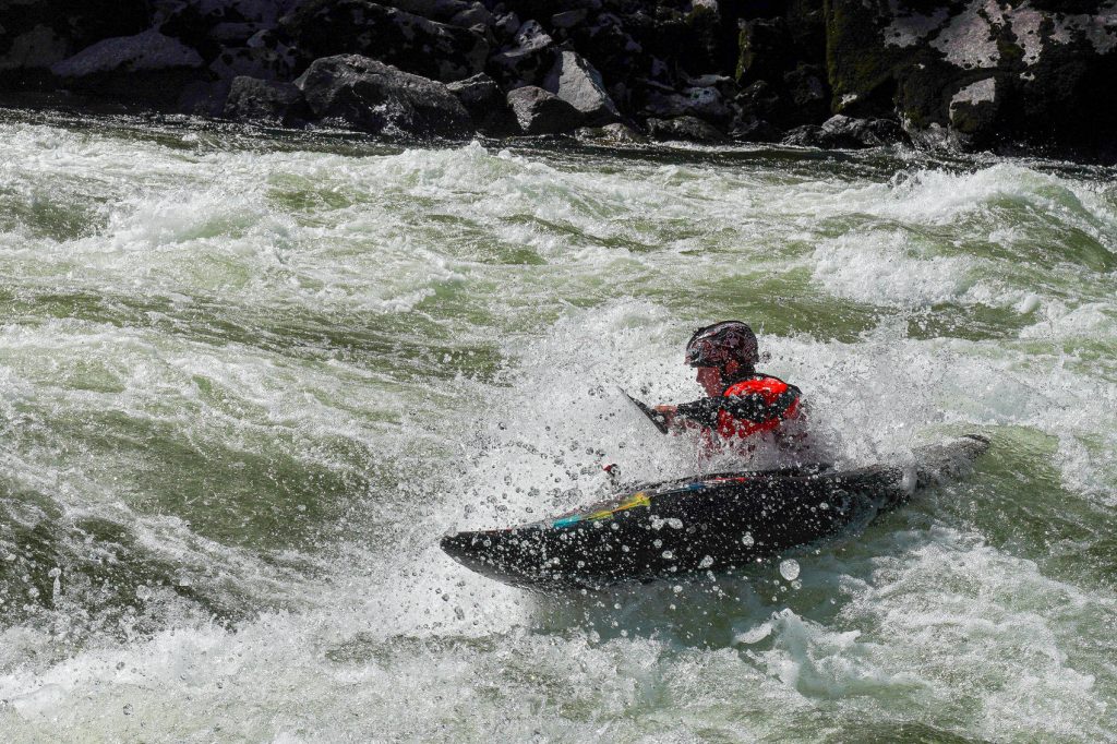 Whitewater kayaker paddling through churning river rapids in Idaho